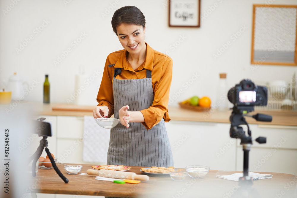 Waist up portrait of beautiful young woman looking at camera while filming baking tutorial for video channel, copy space Waist up portrait of beautiful young woman looking at camera while filming baking tutorial for video channel, copy space