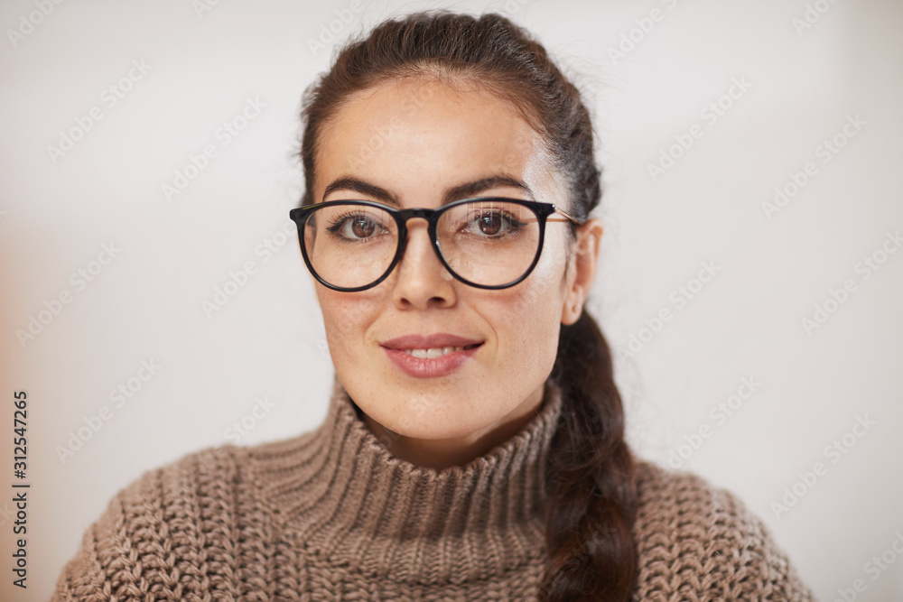 Portrait of contemporary young woman wearing glasses smiling at camera while sitting against plain white background in studio, copy space