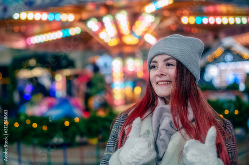 Wallpaper Mural A young beautiful girl with long hair in a fashionable hat and coat, shows a gesture well with two hands in white mittens against the background of the lights of the bokeh night city in winter. Torontodigital.ca