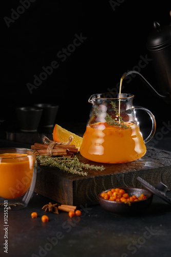 Herbal tea with sea buckthorn in a glass teapot, on wooden board.