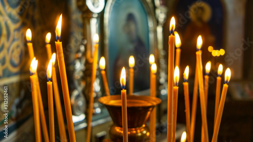Wax burning candles in an orthodox church on the blurred icon background.