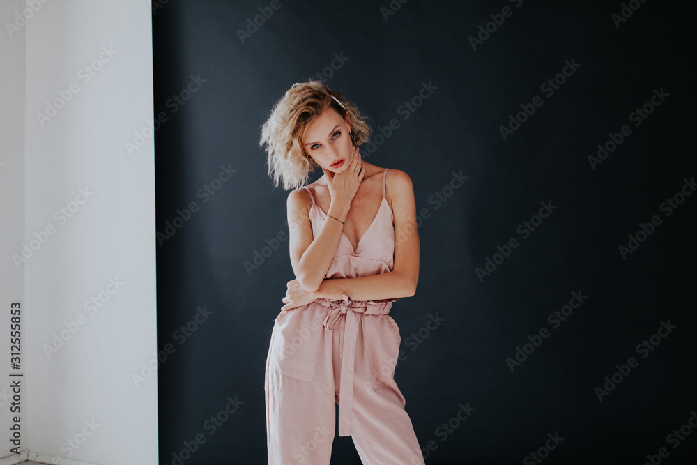 Fototapeta premium Portrait of a beautiful fashionable blonde woman in a pink jumpsuit on a black white background