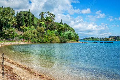 Beautiful landscape with turquoise sea water  green foliage of trees and white clouds on blue sky. Corfu Island  Greece.