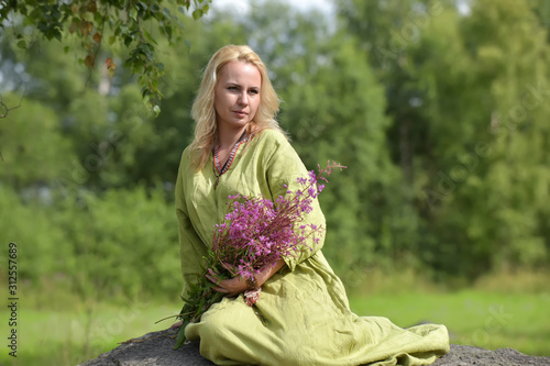 blonde in vintage clothes of the Viking sits with wild flowers in hands photo