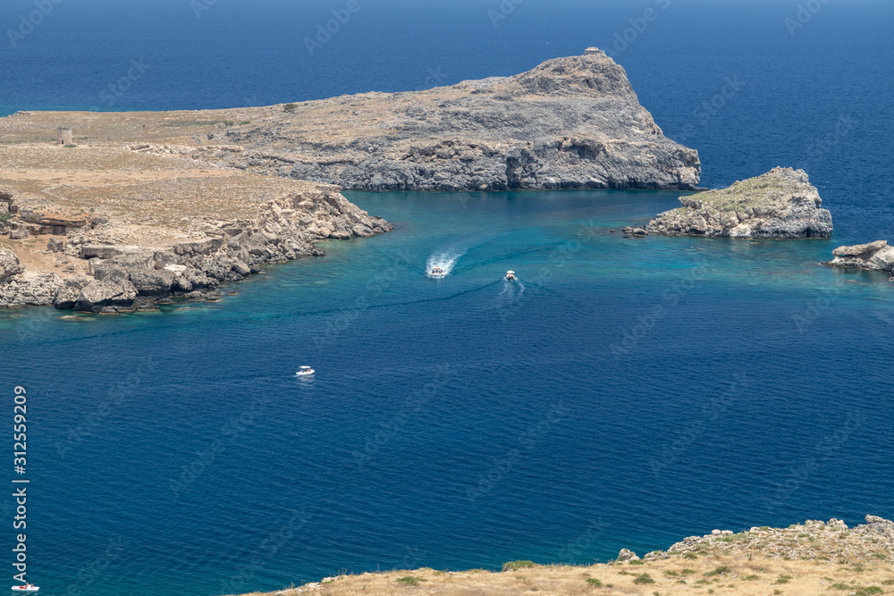 Rocky coastline at Lindos on Greek island Rhodes with rocks in the water , motor boats and the mediterranean sea