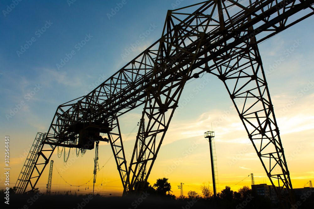 overhead crane at the railway station. Crane silhouette on sunset background. Heavy industry concept. overhead crane at the railway station. Crane silhouette on sunset background. Heavy industry concept.