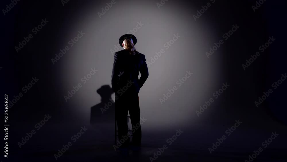 Elegant man in a black hat is dancing an erotic dance. Spotlight on a black background. Elegant man in a black hat is dancing an erotic dance. Spotlight on a black background.