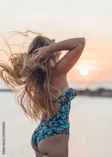 Young woman in swimming suit playing with her hair by the sea in sunset