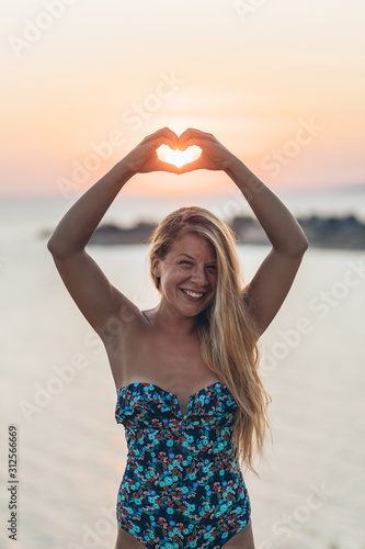 Young woman holding a heart shape into sunset by the sea