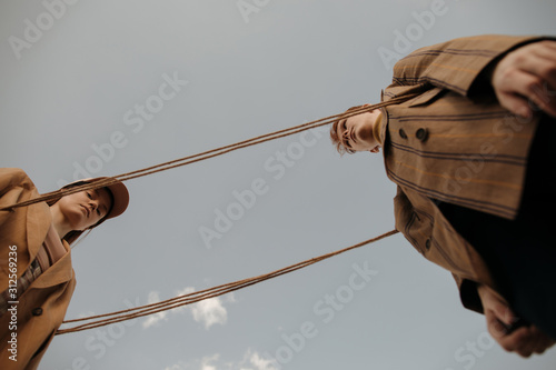 Twins playing with rope against gray sky in countryside