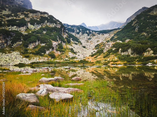 One of the lakes in the Popov Circus of Pirin Mountain, Bulgaria. Rocks, floating flowers and herbaceous plants in summer day. photo