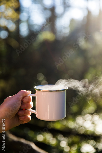 Blank white enamel coffee mug held by a hand in the forest