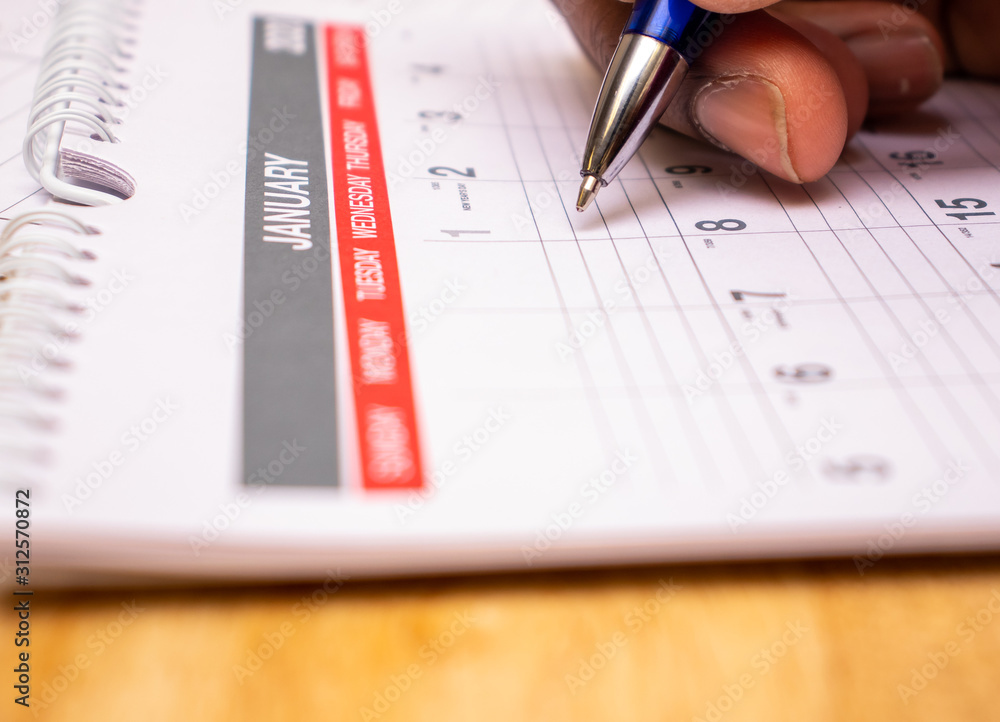 2020 new year concept, african american man with red pen writing plans in calendar for the month of January