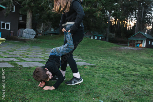 Siblings playing wrestle outside on the grass.