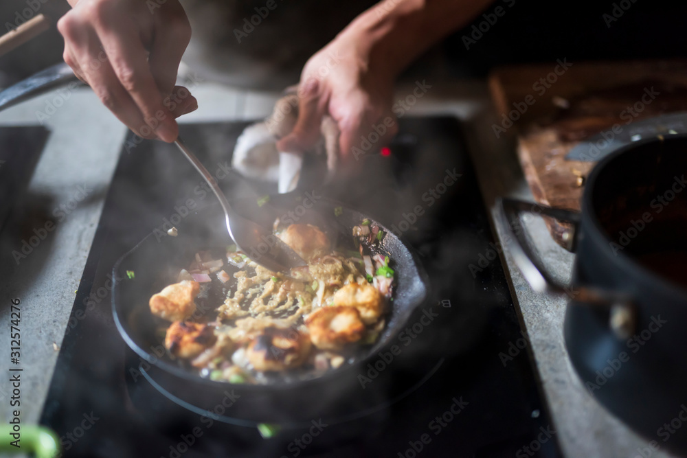 Man cooking delicious food in frying pan on electric stove Man cooking delicious food in frying pan on electric stove