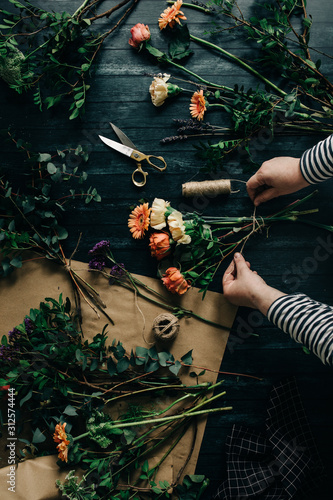 Unknown woman working at florist desk arranging flowers in order to create a bouquet