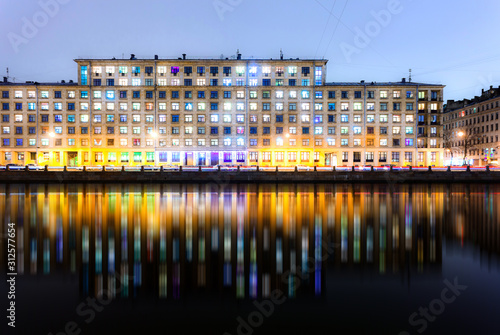 A night view of colourful windows of multifamily houses with their reflections on water