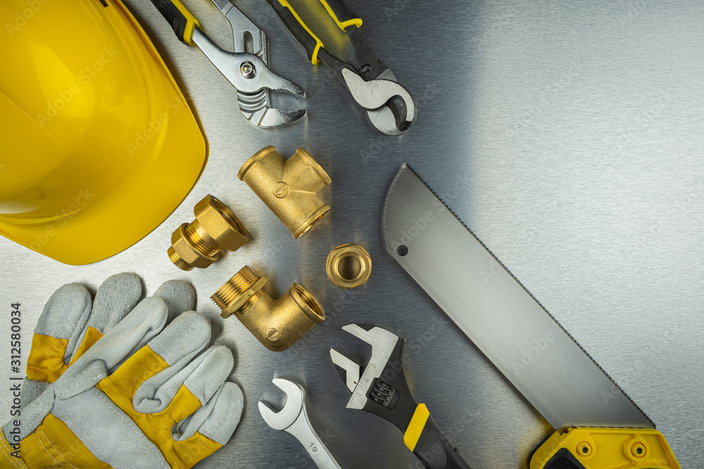 Plumber tools on brushed aluminum background with yellow helmet