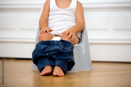 Infant child baby boy toddler sitting on potty, playing with toys in living room