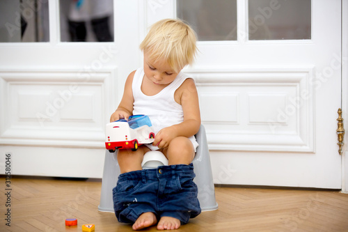 Fotografi Infant child baby boy toddler sitting on potty, playing with toys in living room