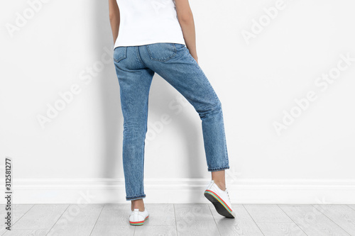 Young woman in stylish jeans near light wall, closeup