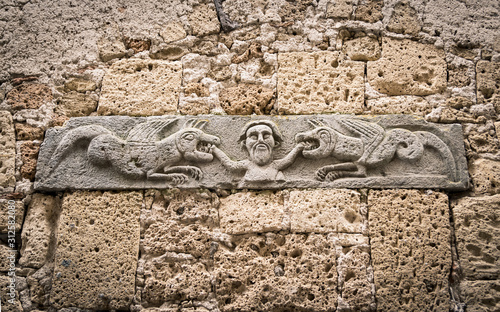 Medieval stone bas-relief depicting a man being devoured by two dragons.