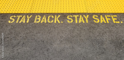Fotografia yellow sign at train station asking people to stay back, stay safe, on concrete