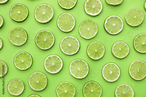 Slices of fresh juicy limes on green background, flat lay