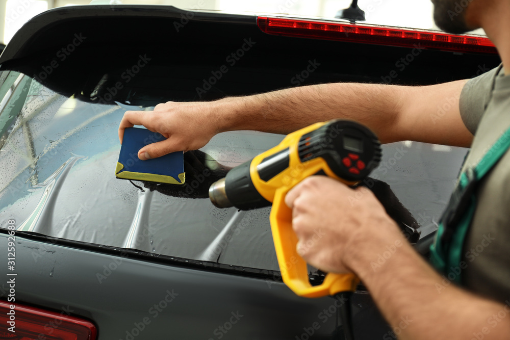 Worker tinting car window with heat gun in workshop, closeup Worker tinting car window with heat gun in workshop, closeup
