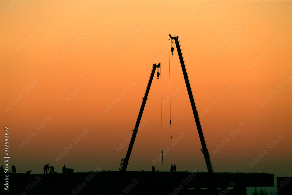 A silhouette of a crane working at a construction site