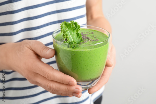Woman holding tasty kale smoothie with chia seeds on light background, closeup
