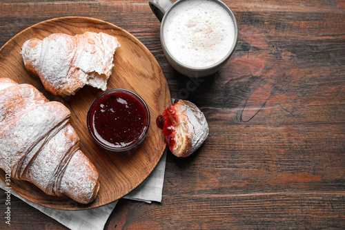 Fresh croissants with jam and coffee on wooden table, flat lay. Space for text