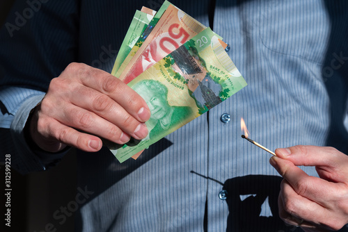 Close-up of man's hands holding burning match near Canadian dollars