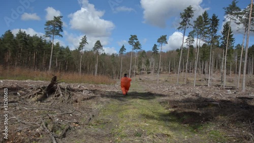 woman in an orange chubby outfit runs throught the forest