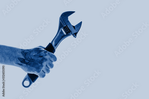 Dirty and oily hand holding adjustable wrench tool colored in trendy color of year 2020 Classic Blue isolated on blue