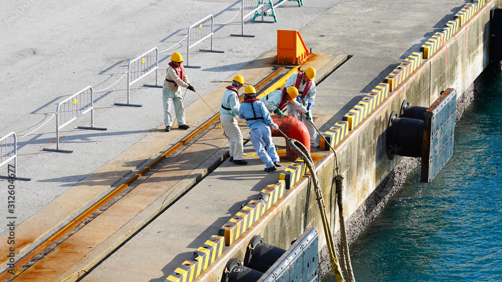 a group of Japanese port workers in uniform and orange helmets fasten ship mooring ropes to the bollard in the port. workers moor ship a group of Japanese port workers in uniform and orange helmets fasten ship mooring ropes to the bollard in the port. workers moor ship