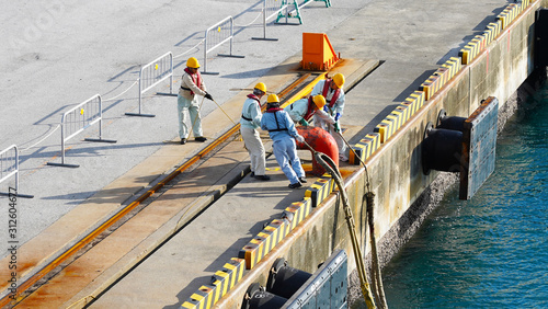a group of Japanese port workers in uniform and orange helmets fasten ship mooring ropes to the bollard in the port. workers moor ship photo