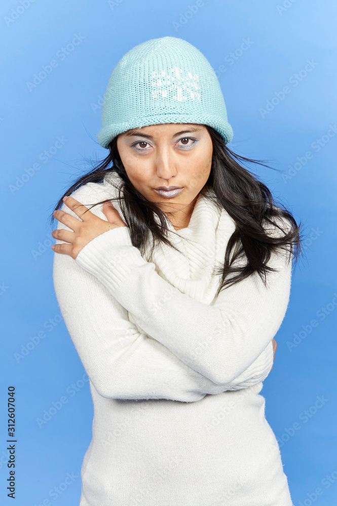 Stunning young Asian woman in winter scene - shot in studio against blue background - wearing thick sweater, cap and with light blue lipstick and eye shadow Stunning young Asian woman in winter scene - shot in studio against blue background - wearing thick sweater, cap and with light blue lipstick and eye shadow