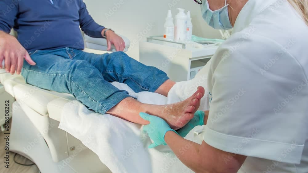 Masseur is gently massaging a middle-aged man's feet in a massage studio. She is using a special cream and blue protection gloves. Masseur is gently massaging a middle-aged man's feet in a massage studio. She is using a special cream and blue protection gloves.