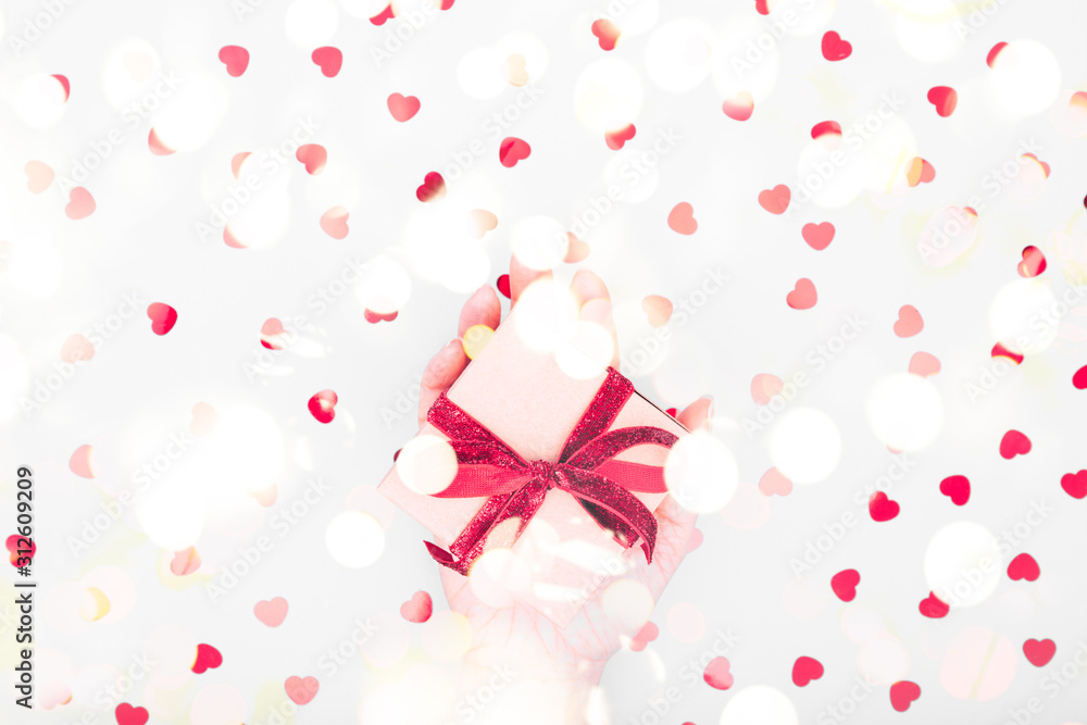Craft box with red ribbon bow in female hand. Valentine day and eco-friendly wrapping concept. Trendy minimalistic flat lay design background. Horizontal with festive bokeh lights Craft box with red ribbon bow in female hand. Valentine day and eco-friendly wrapping concept. Trendy minimalistic flat lay design background. Horizontal with festive bokeh lights