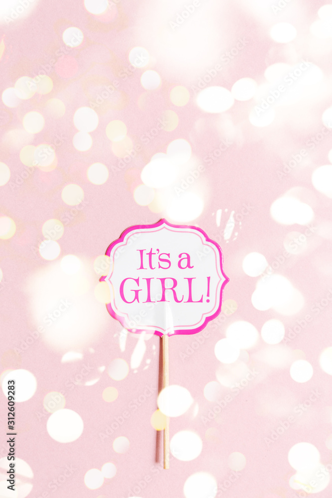 It's a girl sign at the baby shower party. Pink solid background. Baby shower celebration concept. Minimalistic party background. Vertical Top view with festive holiday bokeh