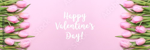 Happy Valentines Day wording with pink tulips on the pink background. Flat lay, top view. Valentines background. Horizontal, banner format