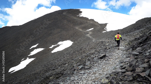 A runner on the trail climbing a stone path to the top of the mountain. Ultra trail running, sporting events, mountain trails marathon.