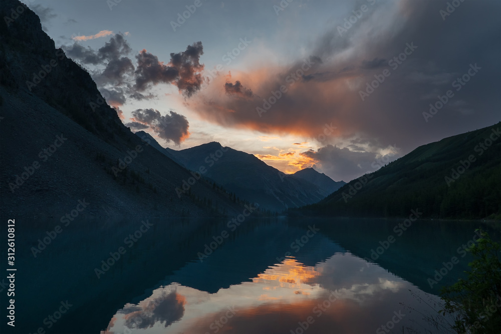 Beautiful landscape with high cliffs with illuminated peaks, water and reflections, blue sky and sunset red.