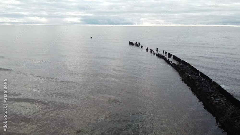 Aerial view of old breakwater - stone pier at Pape beach Baltic sea, Latvia, cloudy and calm day, wide angle establishing drone shot moving backwards Aerial view of old breakwater - stone pier at Pape beach Baltic sea, Latvia, cloudy and calm day, wide angle establishing drone shot moving backwards