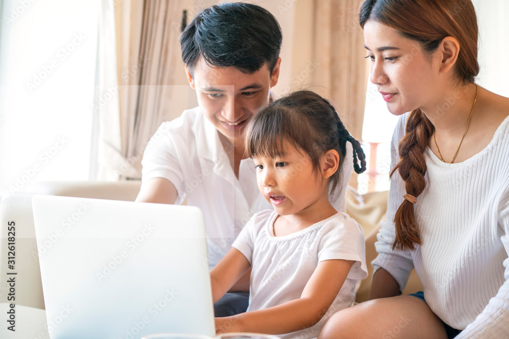 Asian father and mother looking his daughter doing homework with laptop computer in a living room at happy family
