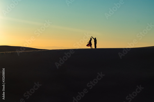 A couple dancing on a desert sand dune at sunset. 