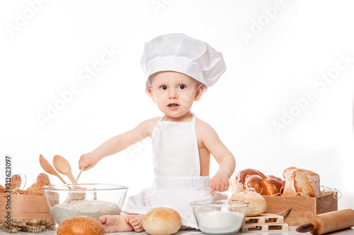 baby cook sits on the table bread bread flour. Little baby chef with bread