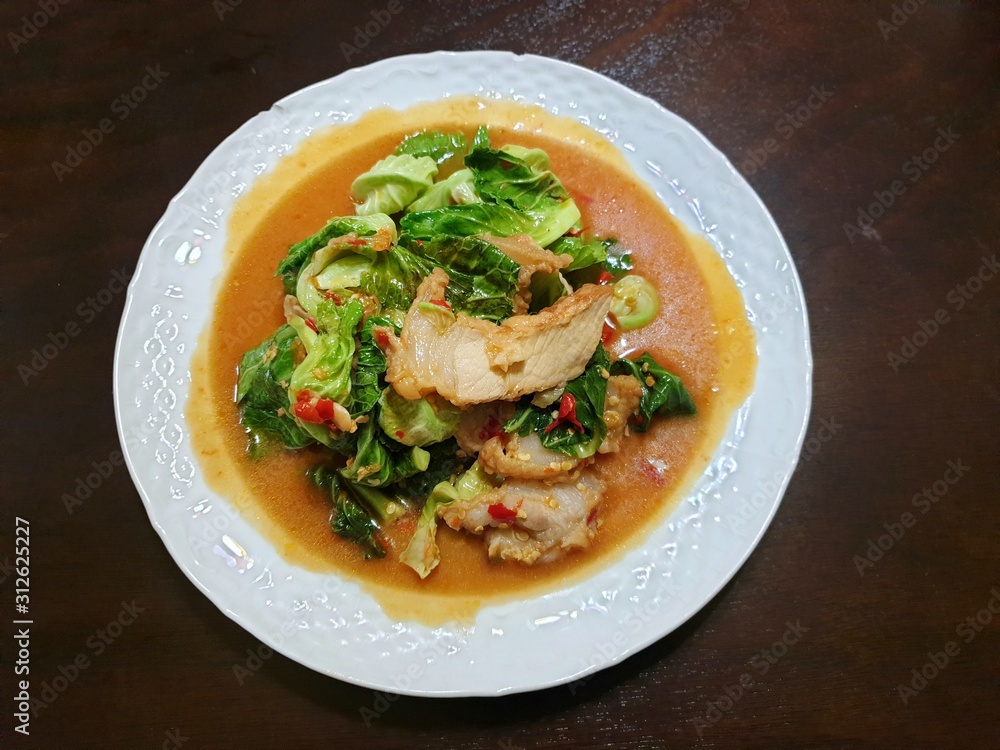 Top view of stir fried cabbage chick topping with fried crispy pork in white plate on wooden table in restaurant, Healthy food concept, Ready to eat or serve Top view of stir fried cabbage chick topping with fried crispy pork in white plate on wooden table in restaurant, Healthy food concept, Ready to eat or serve