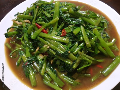 Top view of fried water spinach seasoned with chili and soy sauce on white plate as a background, Stir fried swamp cabbage or chinese morning glory, Pad pak boong is Thai traditional, Ready to eat photo